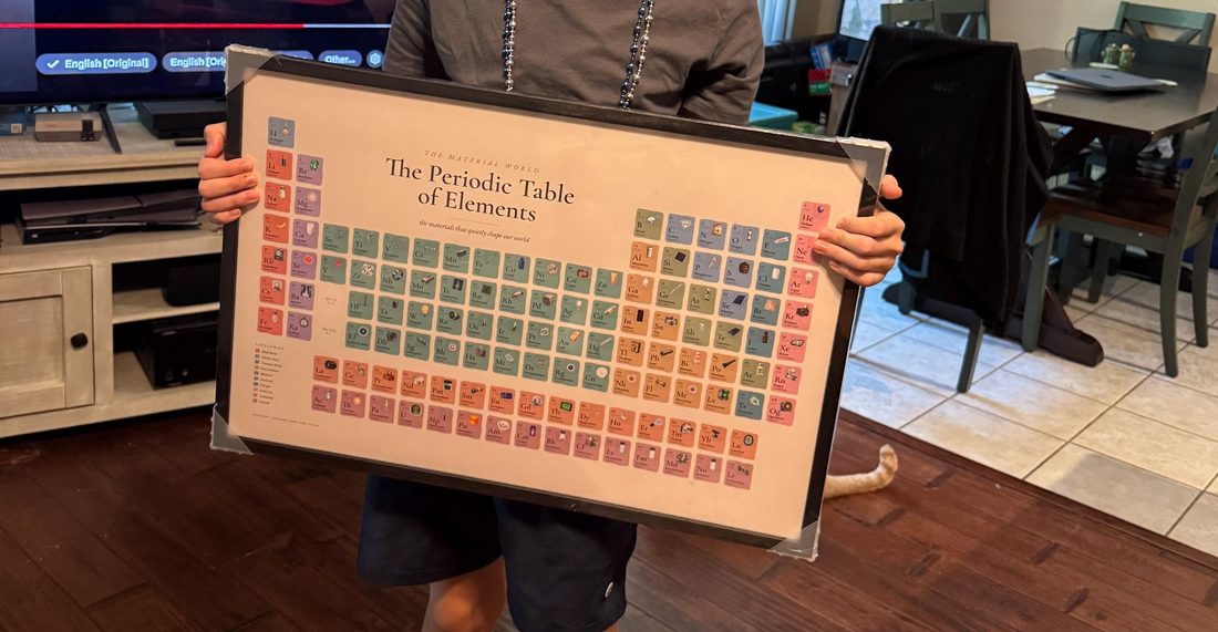 A customer holding the framed Periodic Table of Elements poster at home